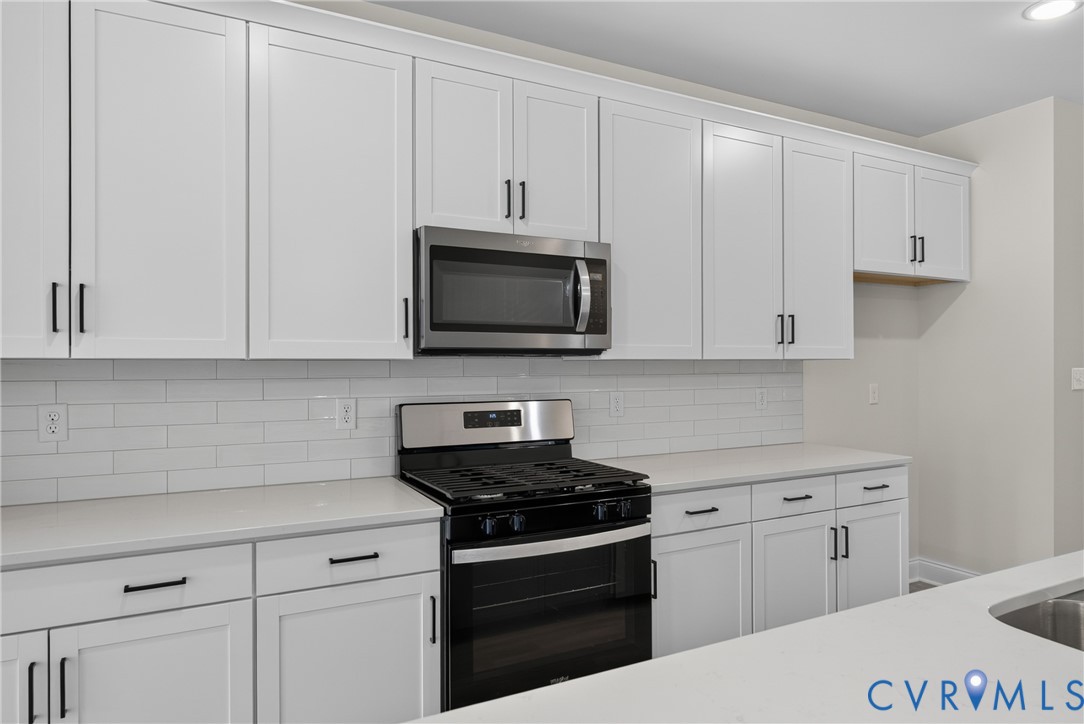 White shaker cabinetry, stainless steel appliances, subway tile backsplash, light-toned countertops, and matte black hardware
