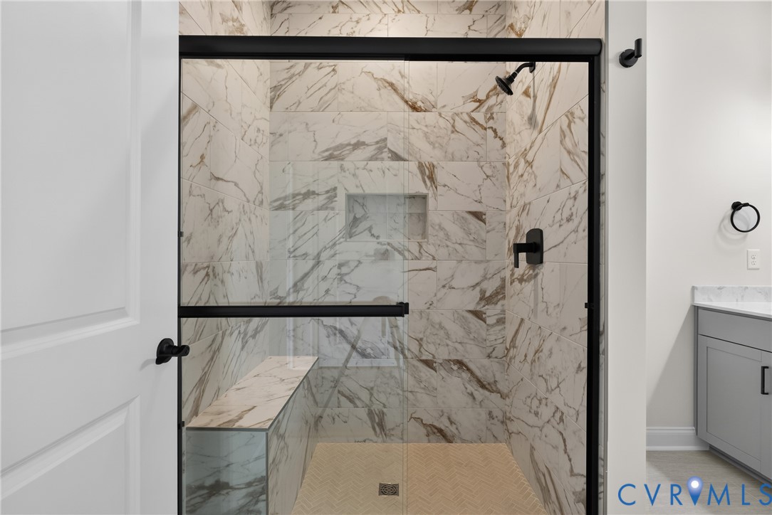 Glass-enclosed shower with matte black fixtures, full-height tile surround, built-in bench, and a recessed niche