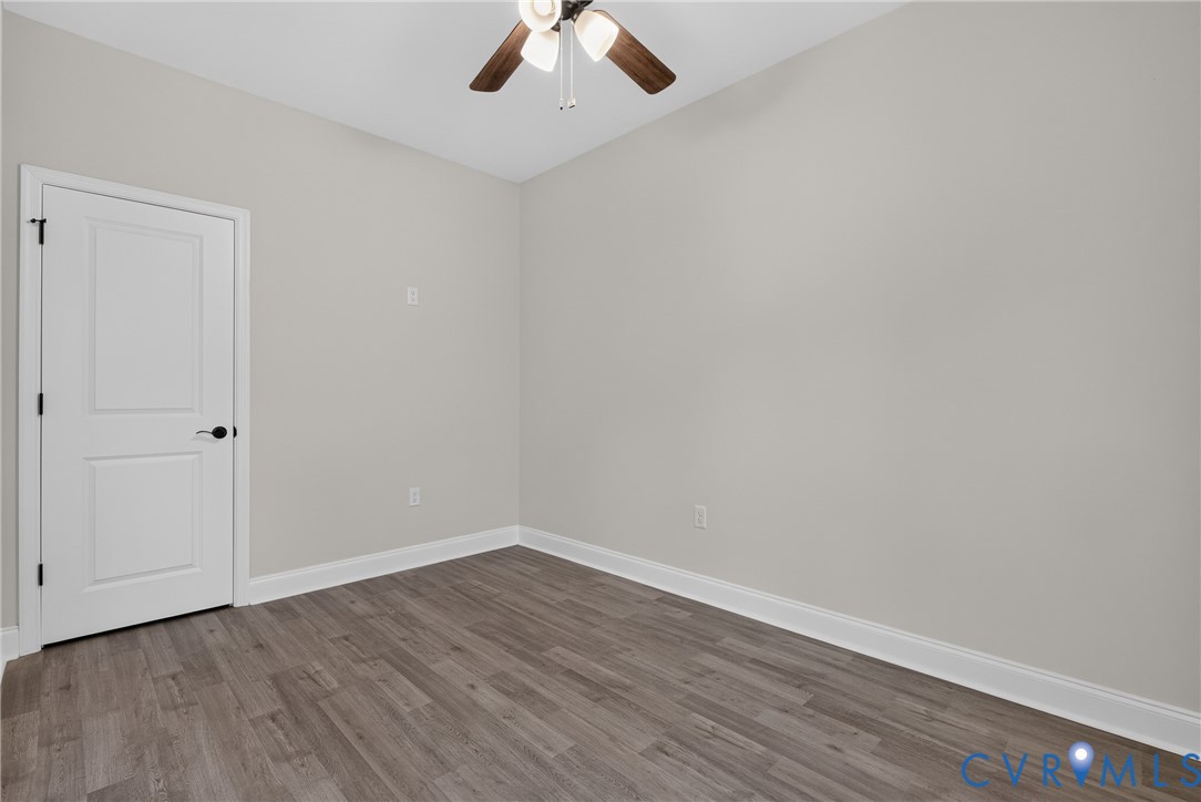 Wood-finish flooring, white paneled door with matte black hardware, and a ceiling fan with light fixture