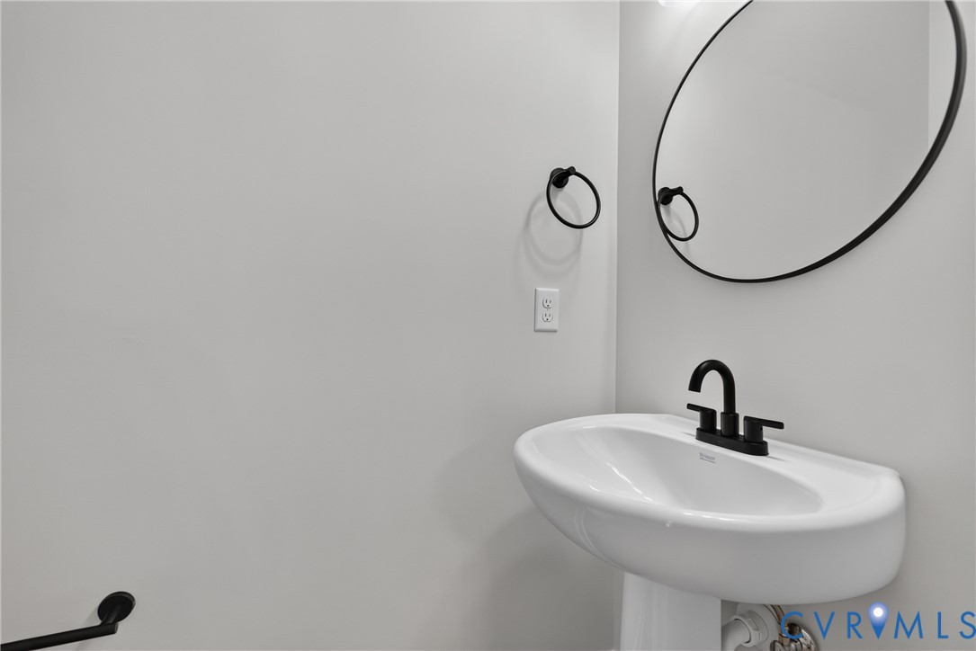 Pedestal sink with a matte black two-handle faucet, round wall mirror, and matte black towel rings