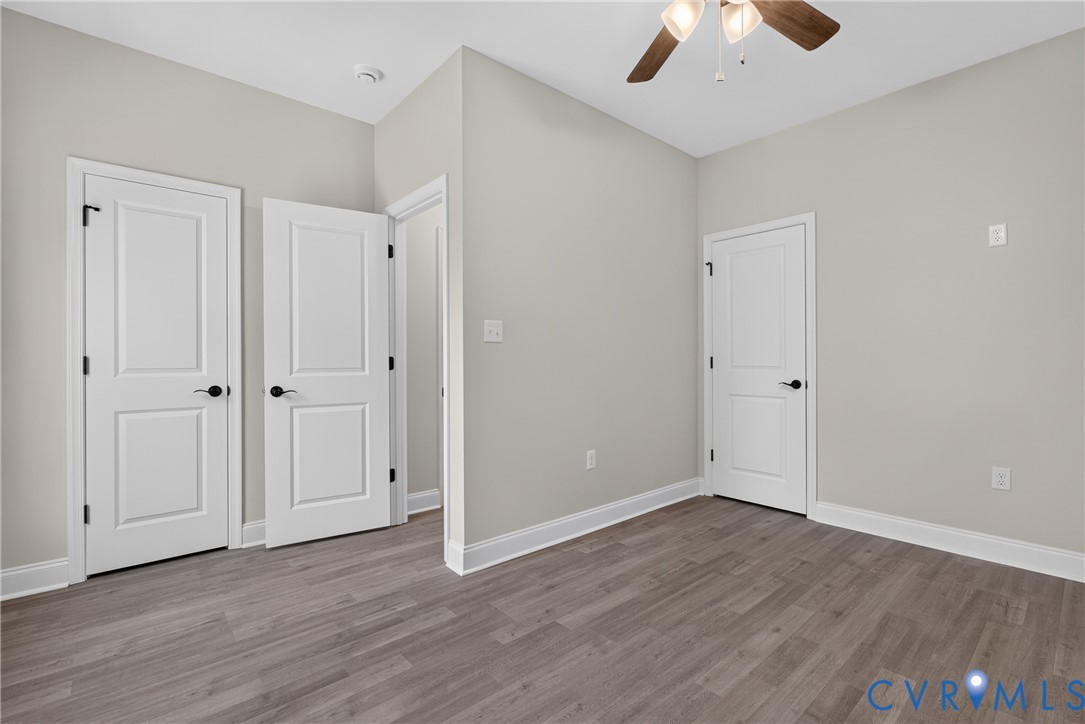 Light gray wall paint, wood-finish flooring, white paneled doors with black hardware, and a ceiling fan with integrated lighting