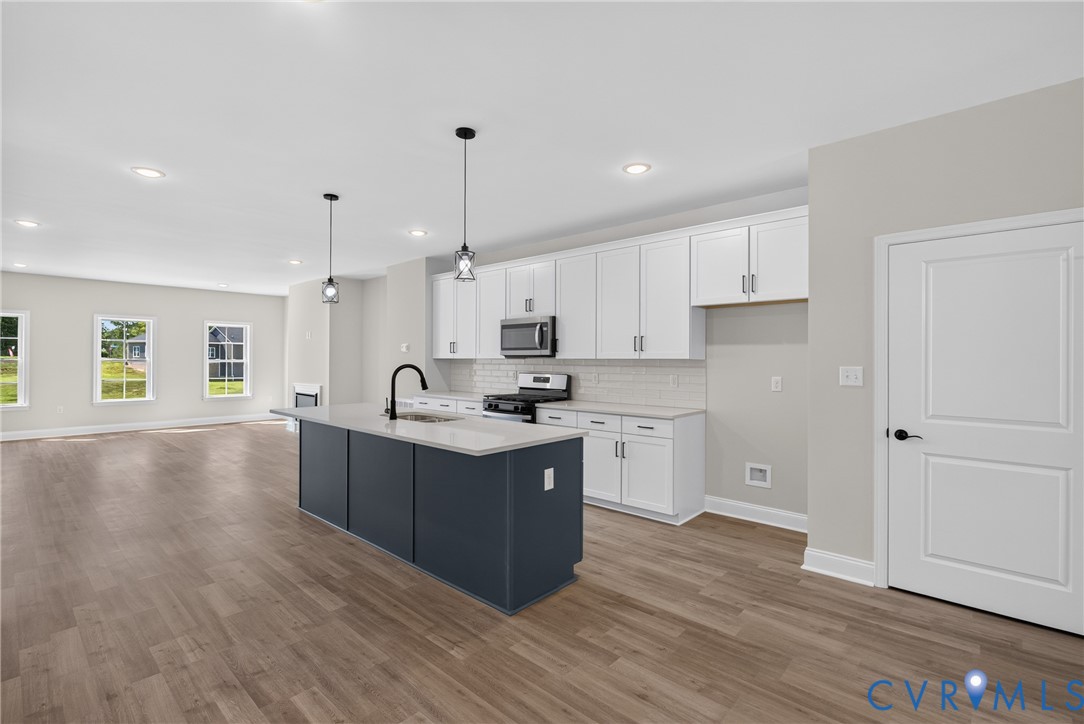 Open-concept kitchen with a central island, white cabinetry, integrated stainless steel appliances, and wood-finish flooring