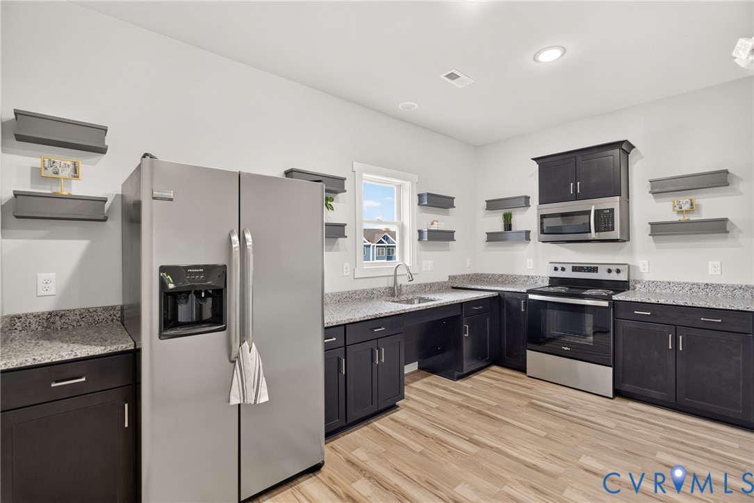 Kitchen with wood-finish flooring, dark cabinetry, light-toned countertops, stainless steel appliances, and a window above the sink
