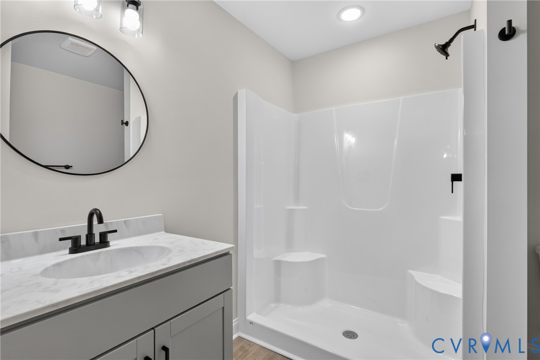 Vanity with an integrated sink and stone-finish countertop, matte black faucet, framed round mirror, overhead vanity lighting, and a walk-in shower with built-in seating Vanity with an integrated sink and stone-finish countertop, matte black faucet, framed round mirror, overhead vanity lighting, and a walk-in shower with built-in seating
