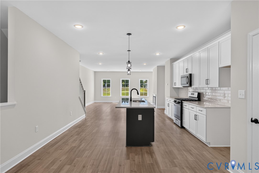Kitchen featuring a central island with sink, stainless steel appliances, white cabinetry, and wood-finish flooring
