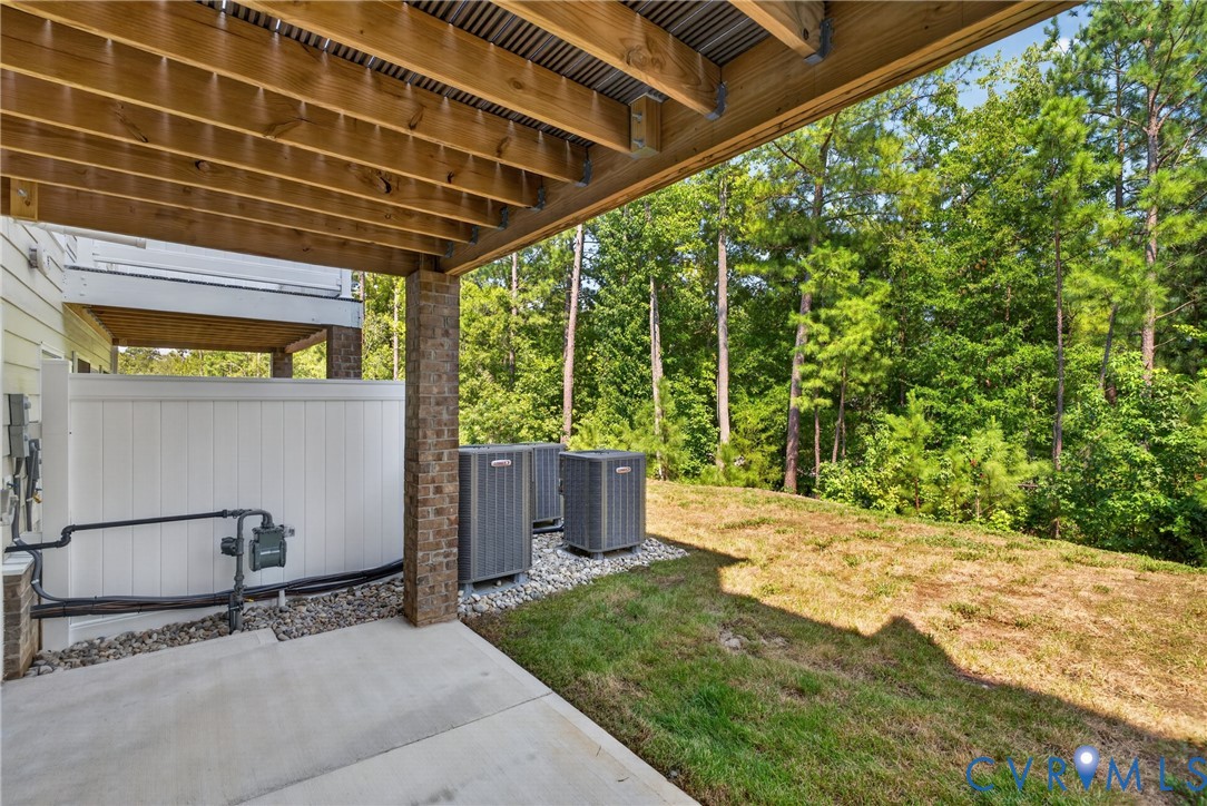 Concrete patio with wood-finish ceiling, brick support columns, and green space