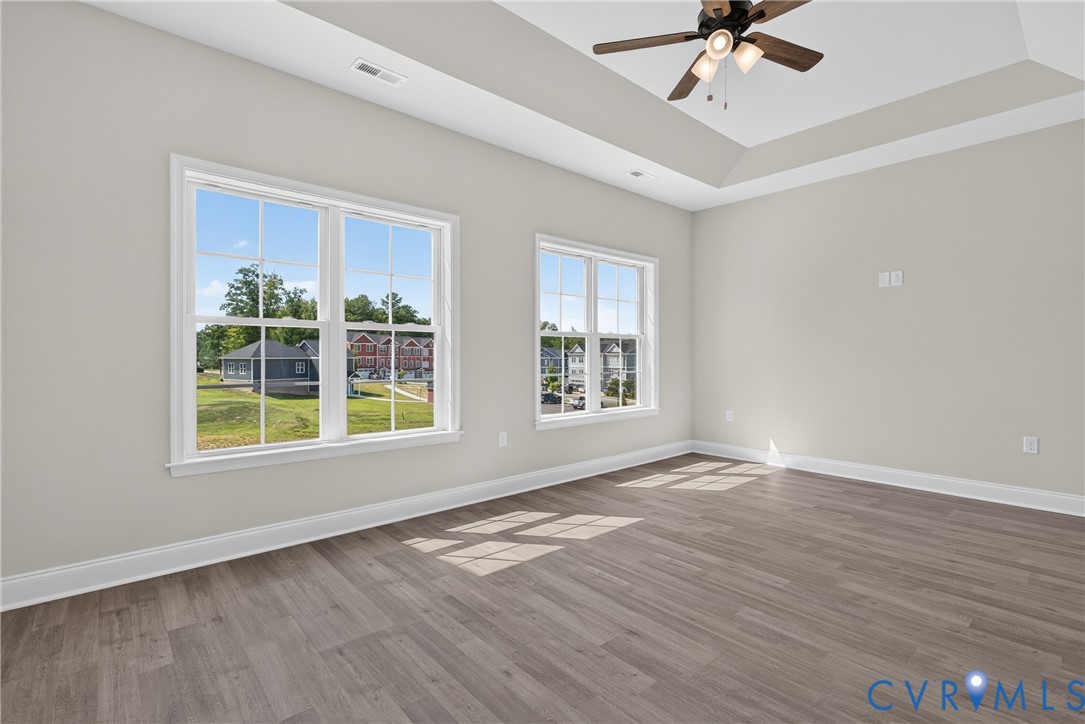 Tray ceiling, wood-finish flooring, two large windows, white trim, and a ceiling fan