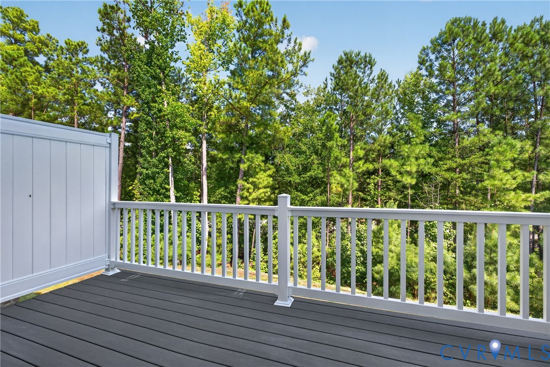 Composite decking with a privacy wall and white baluster railing, set against a backdrop of mature trees