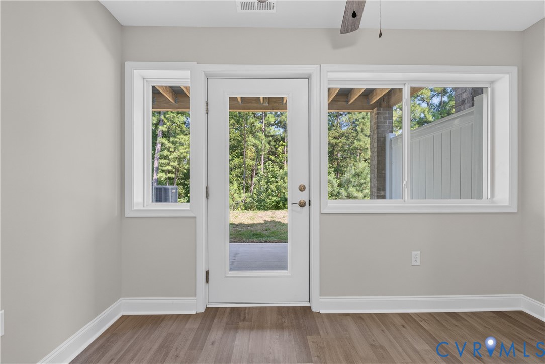 Wood-finish flooring, light grey wall paint, multiple windows, and a glass-paneled exterior door Wood-finish flooring, light grey wall paint, multiple windows, and a glass-paneled exterior door