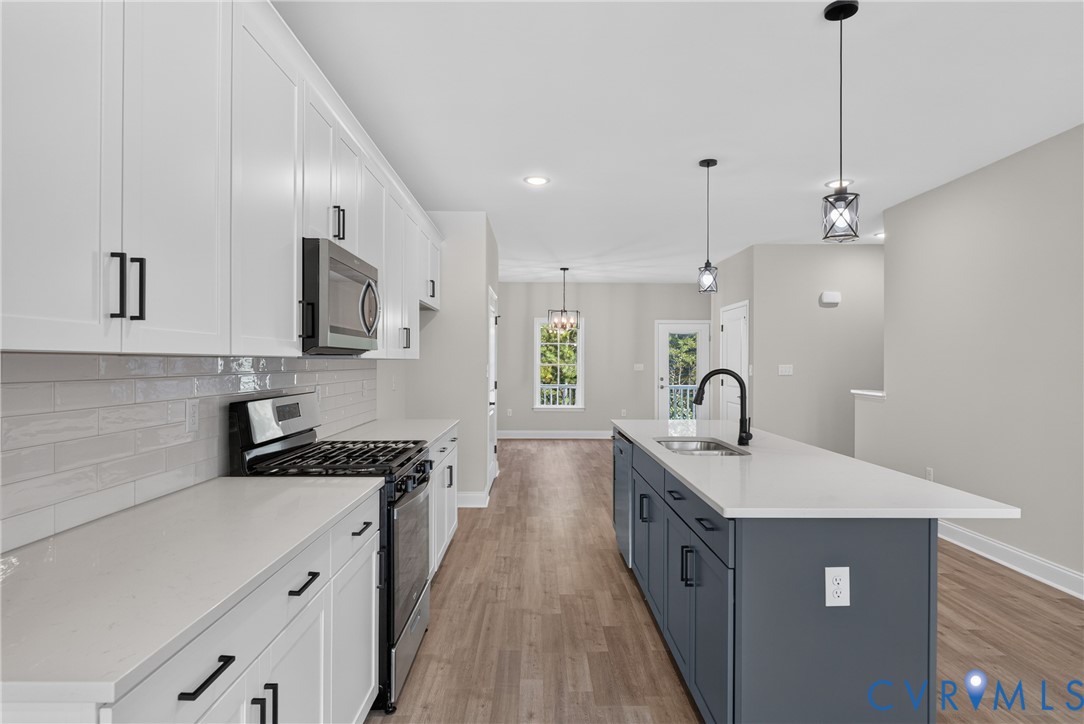 Kitchen featuring white cabinetry, light gray subway tile backsplash, stainless steel appliances, a center island with a sink, and wood-finish flooring