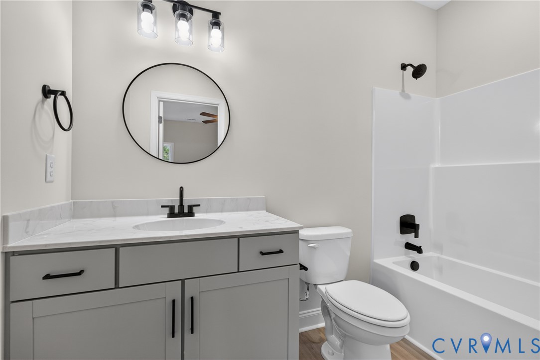 Bathroom featuring a white integrated sink, light gray vanity with black hardware, black-framed round mirror, and a tub/shower combination with black fixtures