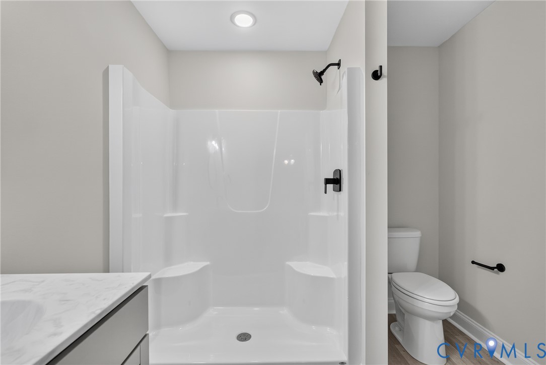 Integrated shower unit with built-in seating, matte black shower fixtures, recessed lighting, and a white toilet Integrated shower unit with built-in seating, matte black shower fixtures, recessed lighting, and a white toilet