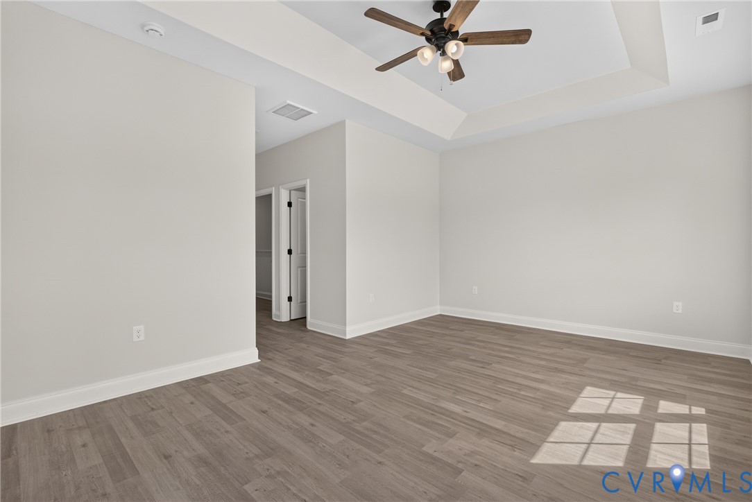 Tray ceiling with an attached ceiling fan, light wood-finish flooring, and crisp white baseboards