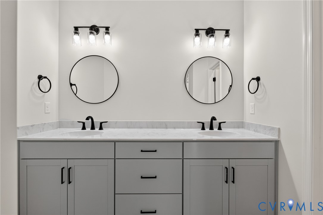 Double vanity with stone countertop, undermount sinks, matte black fixtures, and circular mirrors