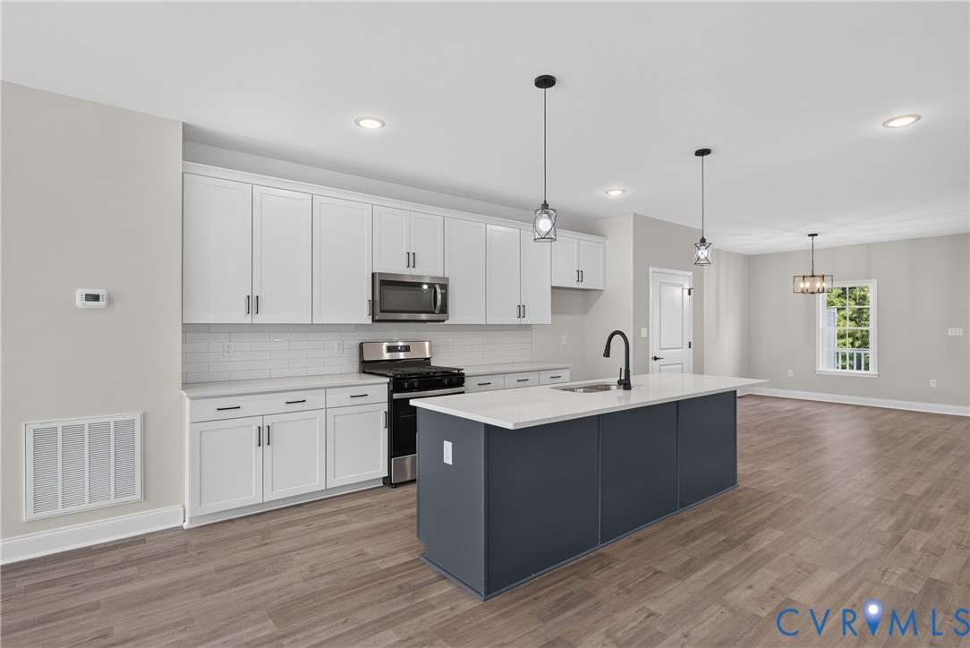 Kitchen featuring white cabinetry, subway tile backsplash, stainless steel appliances, a center island with a sink, and wood-finish flooring