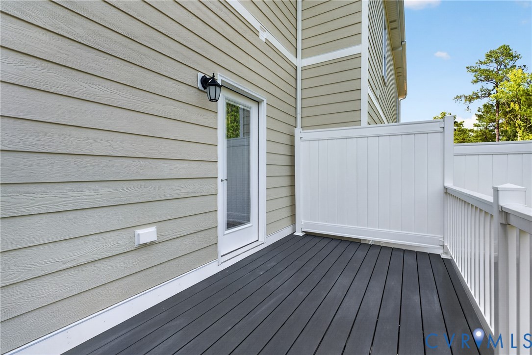 Deck featuring dark grey composite flooring, white railing, and a privacy wall, with a white exterior door leading to the interior