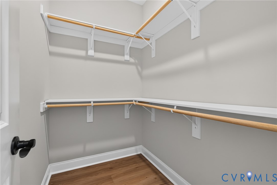 Walk-in closet with wood-finish flooring, white shelving, and wood rods