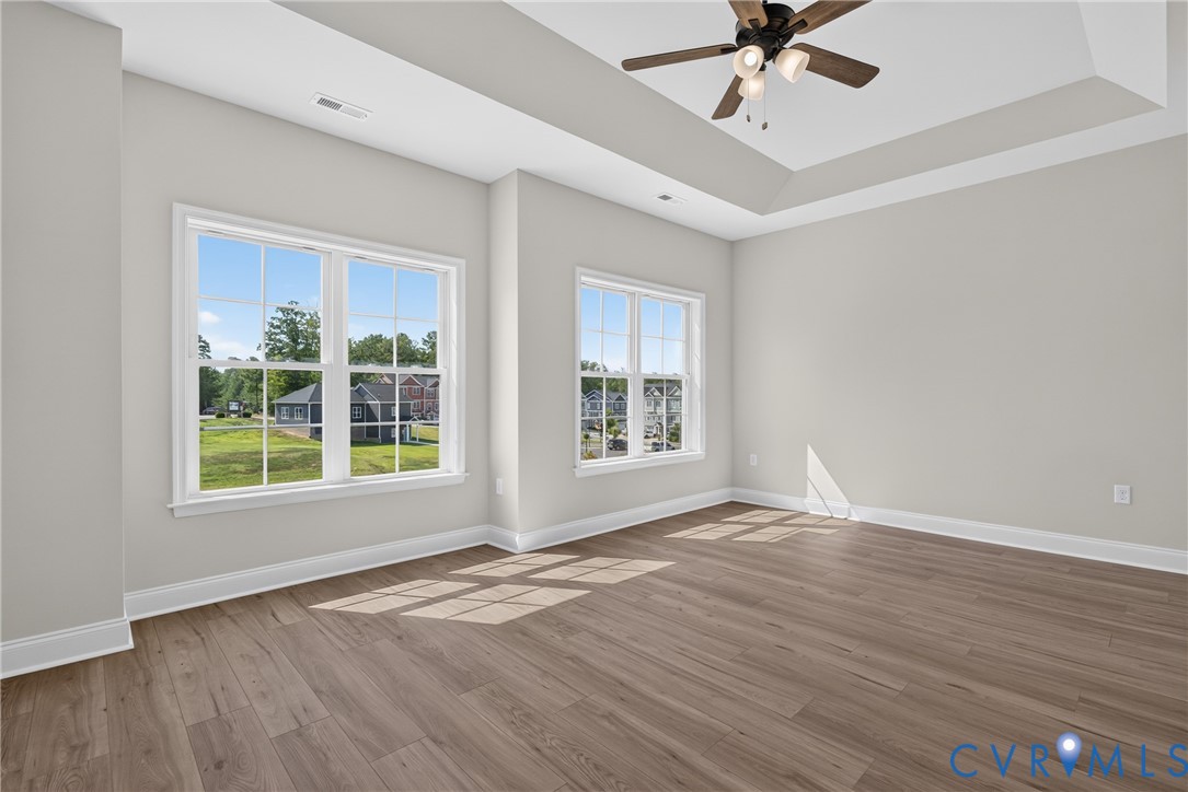 Tray ceiling with a ceiling fan, wood-finish flooring, and multiple windows