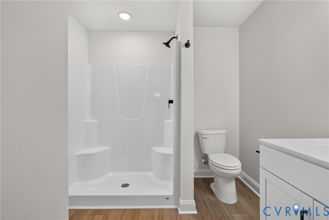 Walk-in shower with integrated seating, matte black shower fixtures, wood-finish flooring, white vanity with integrated sink, and white toilet Walk-in shower with integrated seating, matte black shower fixtures, wood-finish flooring, white vanity with integrated sink, and white toilet