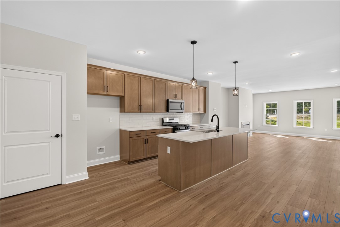 Open concept kitchen featuring wood-finish flooring, recessed lighting, a kitchen island with pendant lighting, and a subway tile backsplash Open concept kitchen featuring wood-finish flooring, recessed lighting, a kitchen island with pendant lighting, and a subway tile backsplash
