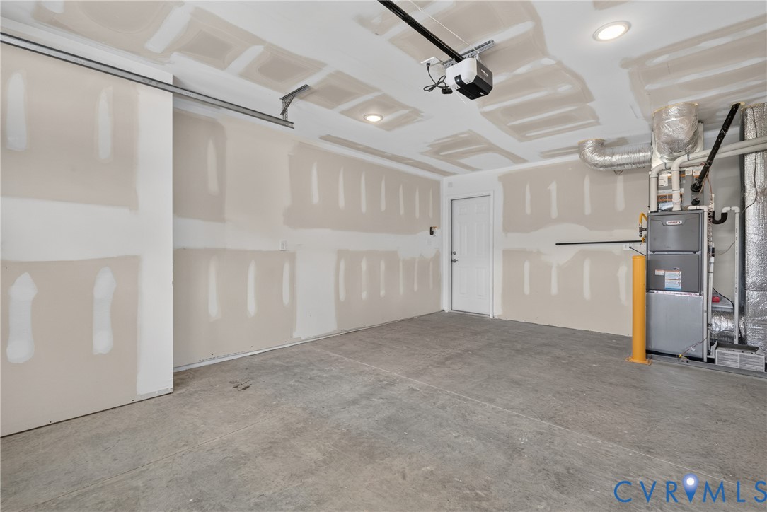 Unfinished garage with a concrete floor, built-in overhead garage door opener, and recessed ceiling lighting