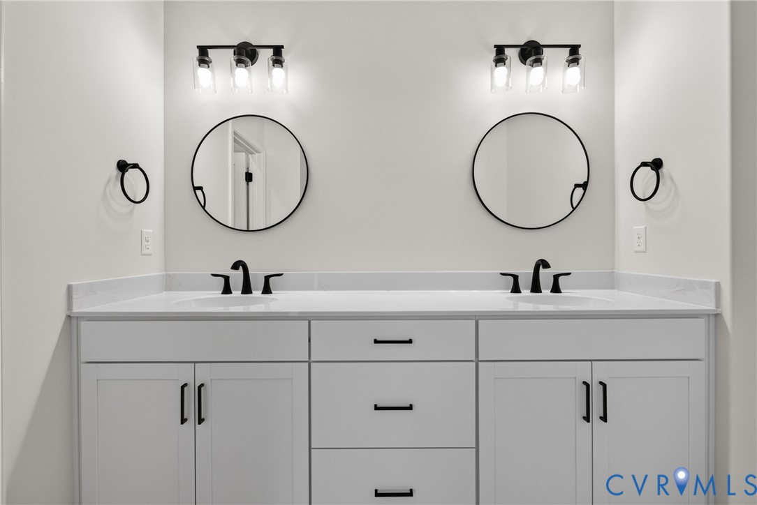 Dual white vanities with integrated sinks, white countertops, matte black faucets, and round mirrors