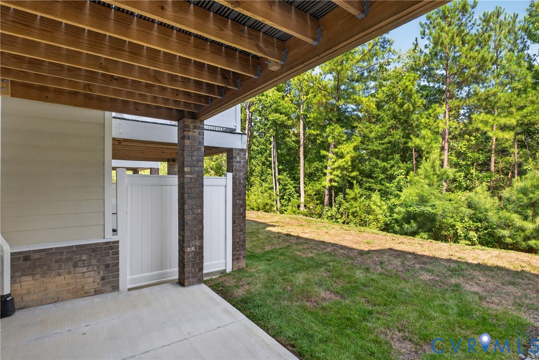 Concrete patio with a wood-framed deck overhead, brick pillar accents, and a privacy fence
