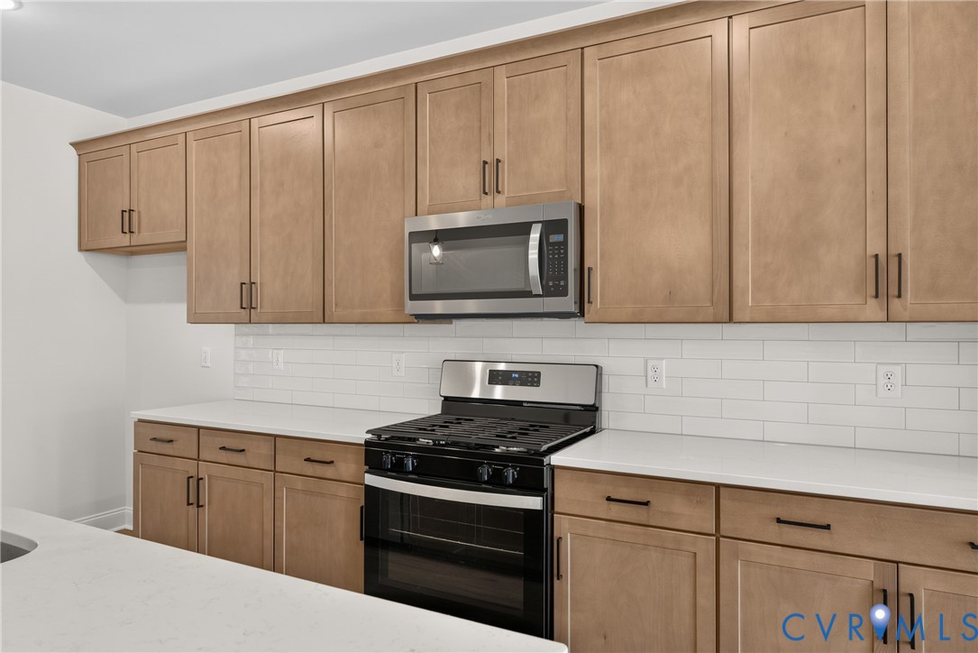 Stainless steel microwave, stainless steel range with oven, white subway tile backsplash, light wood-finish cabinetry, and white countertops
