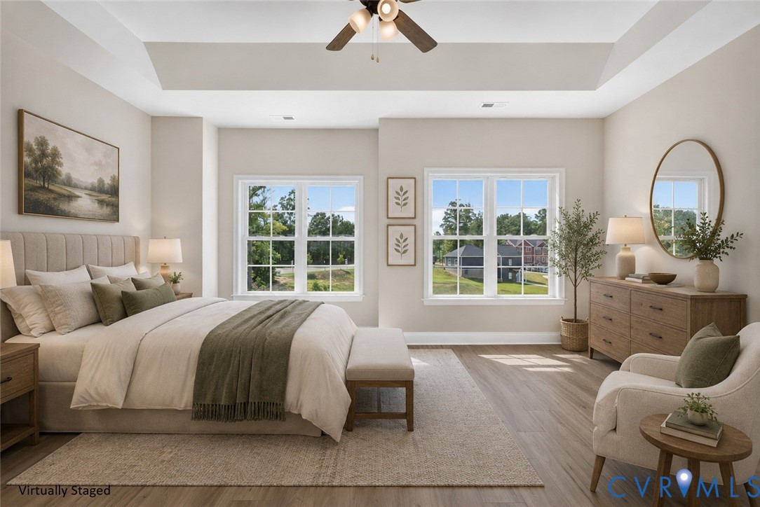 Recessed tray ceiling with ceiling fan, wood-finish flooring, and multiple double-pane windows