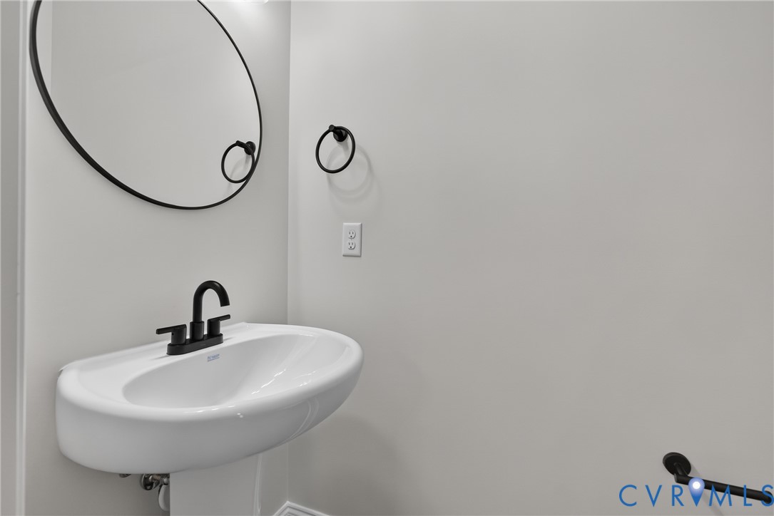 Pedestal sink with a matte black faucet, wall-mounted mirror, and complementary towel rings