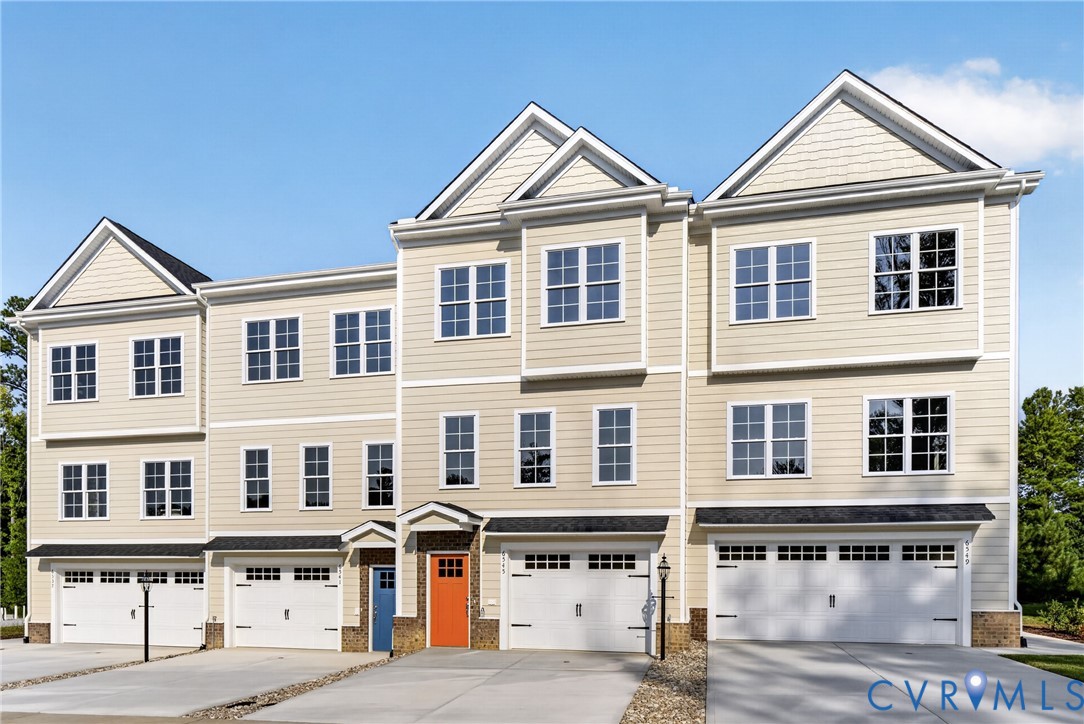 Multi-story facade featuring light-toned siding, white-framed windows, and individual garage doors