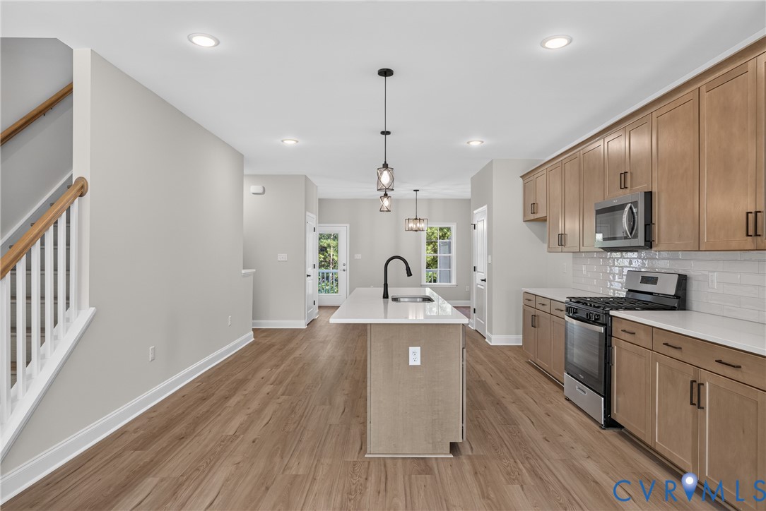 Open-concept living space with wood-finish flooring, recessed lighting, and a staircase with white spindles and a wood handrail