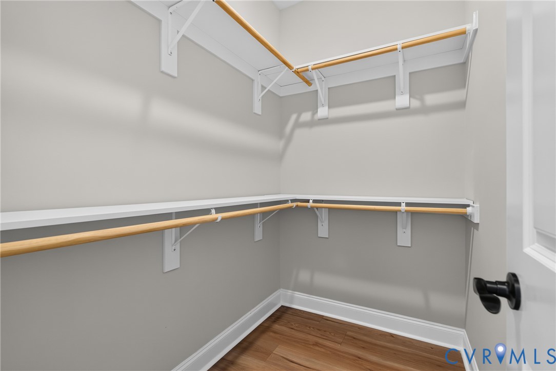 Walk-in closet with wood-finish flooring, white shelving, and wood hanging rods