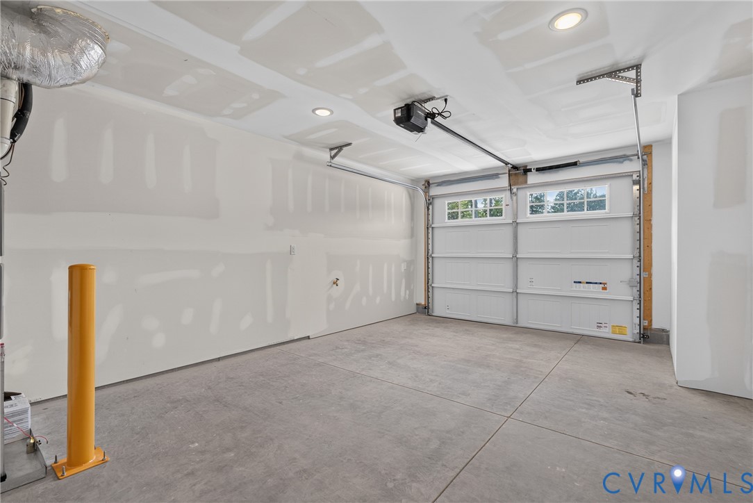 Concrete flooring, recessed lighting, white panel garage door, automatic garage door opener, and a yellow bollard