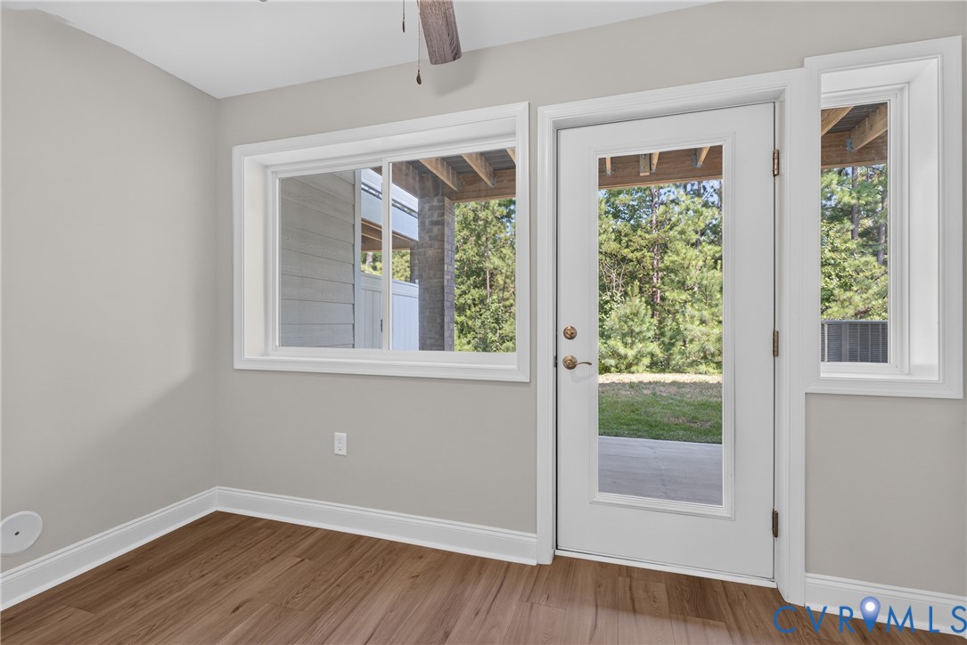Wood-finish flooring, light gray wall paint, white trim, glass-paned door, and large windows offering exterior visibility Wood-finish flooring, light gray wall paint, white trim, glass-paned door, and large windows offering exterior visibility