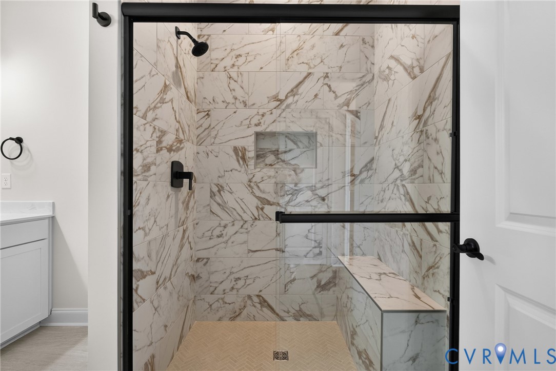 Spacious shower featuring full-height marble-look tile, a built-in bench, and a recessed niche