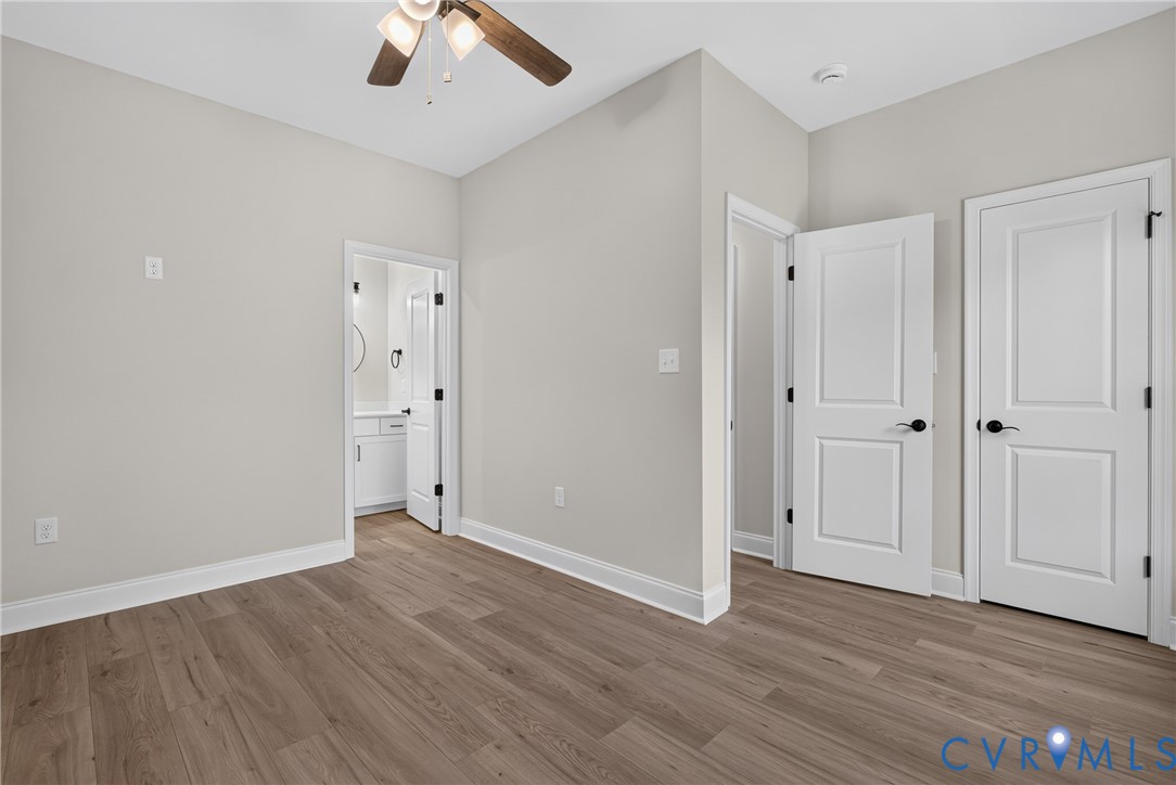 Wood-finish flooring, ceiling fan with integrated lighting, paneled interior doors with matte black hardware, and crisp white trim
