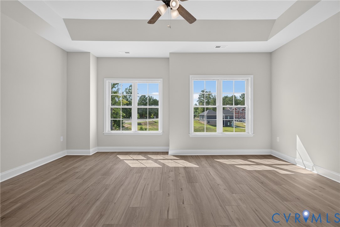 Tray ceiling with a ceiling fan, two windows with white trim, and wood-finish flooring