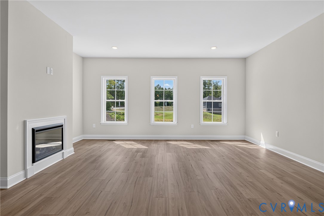 Recessed electric fireplace, wood-finish flooring, three double-hung windows, recessed ceiling lighting, and crisp white trim