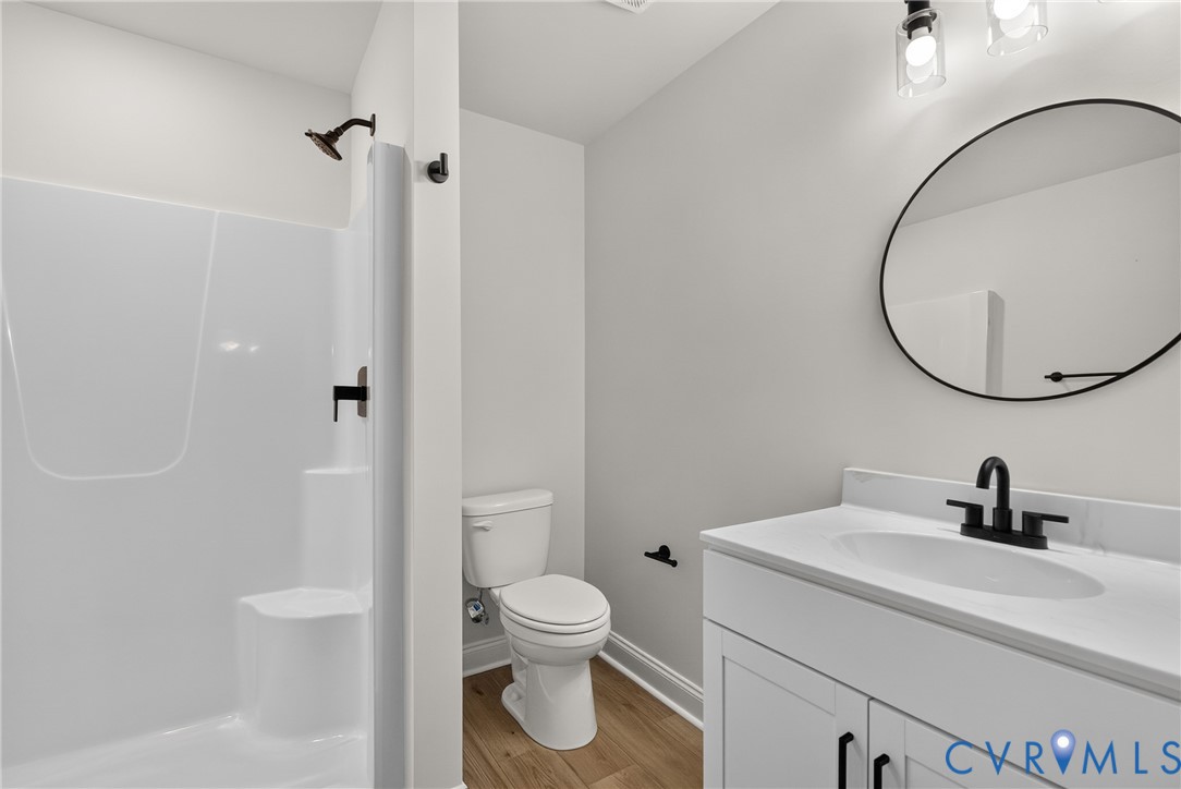 White vanity with integrated sink and matte black faucet, round wall-mounted mirror, and wood-finish flooring White vanity with integrated sink and matte black faucet, round wall-mounted mirror, and wood-finish flooring