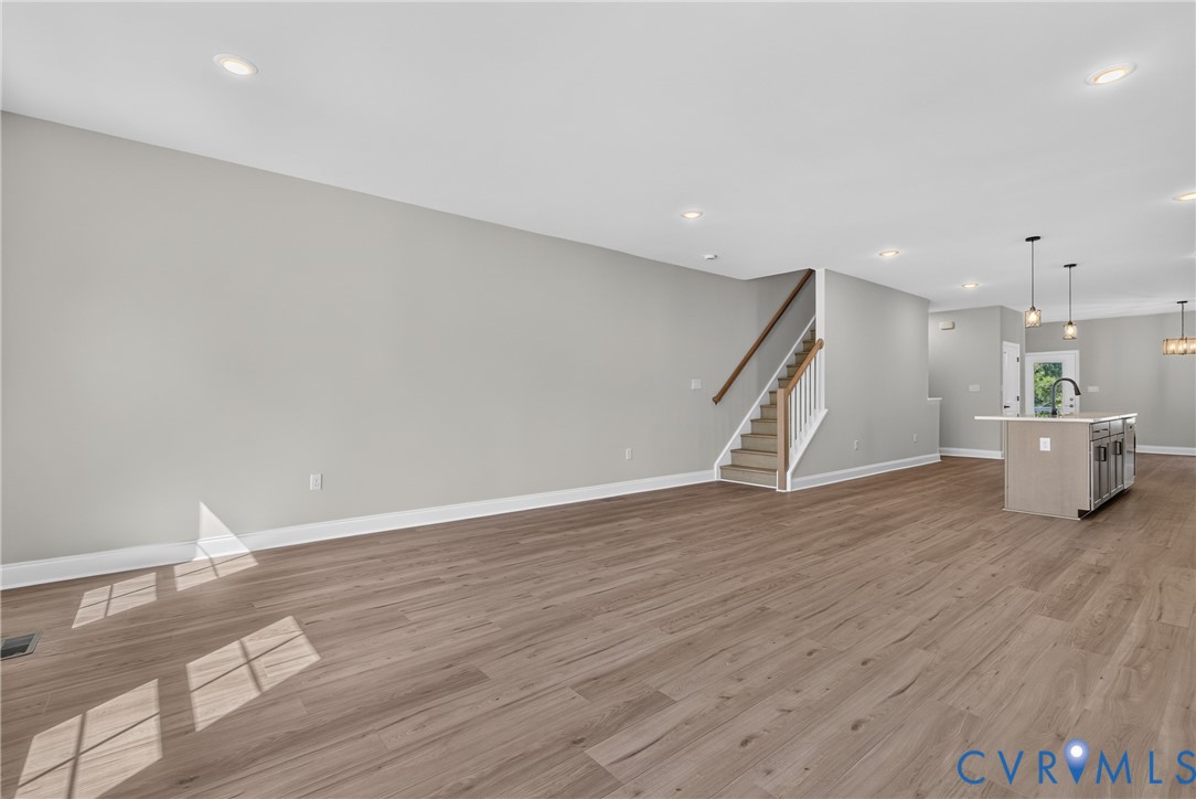Open-concept living space with wood-finish flooring, recessed lighting, and a staircase with wood handrails