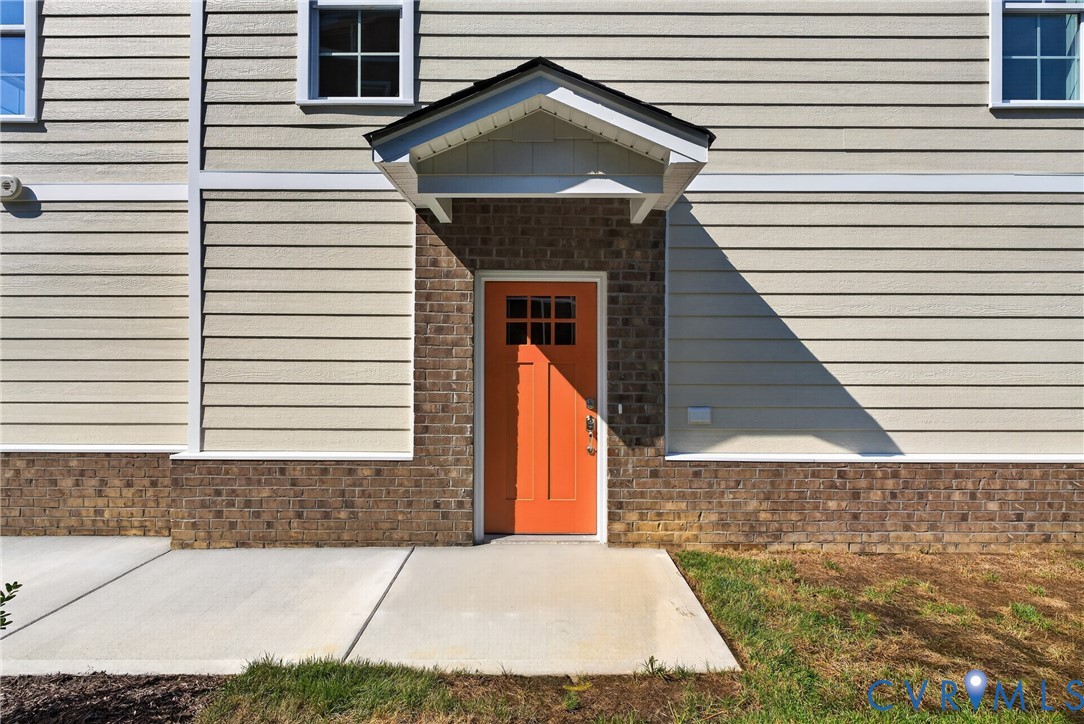 Exterior facade featuring horizontal siding, brick wainscoting, an orange paneled entry door, and a covered entry Exterior facade featuring horizontal siding, brick wainscoting, an orange paneled entry door, and a covered entry