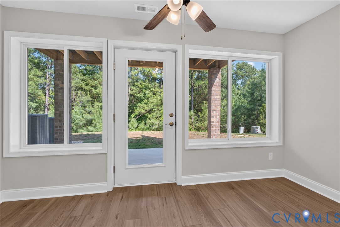 Wood-finish flooring, white trim, ceiling fan, glass-paneled door, and multiple windows Wood-finish flooring, white trim, ceiling fan, glass-paneled door, and multiple windows