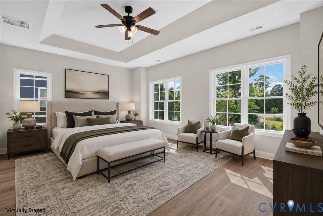 Tray ceiling with a ceiling fan, wood-finish flooring, and multiple windows