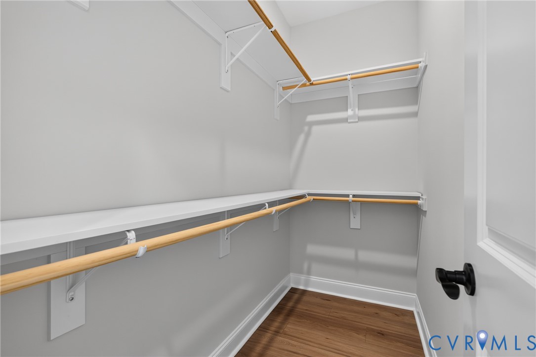 Walk-in closet featuring white shelving, wood-finish hanging rods, and wood-finish flooring