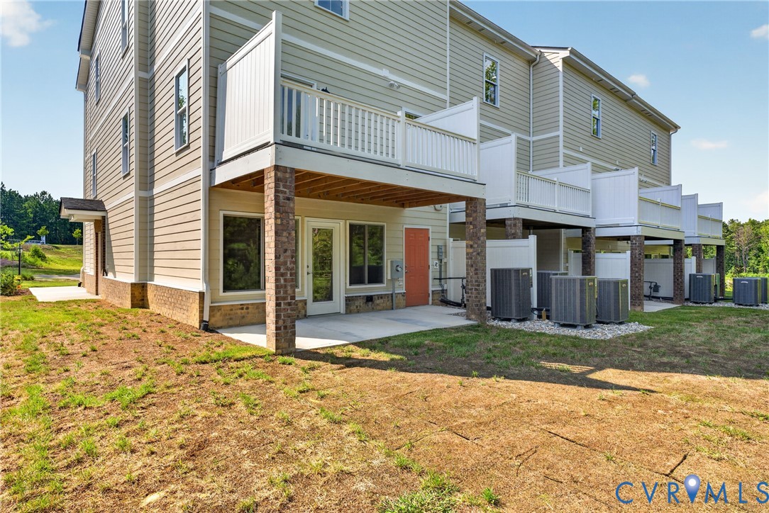 Exterior featuring composite siding, a private balcony with white railings, a ground-level patio, and brick columns