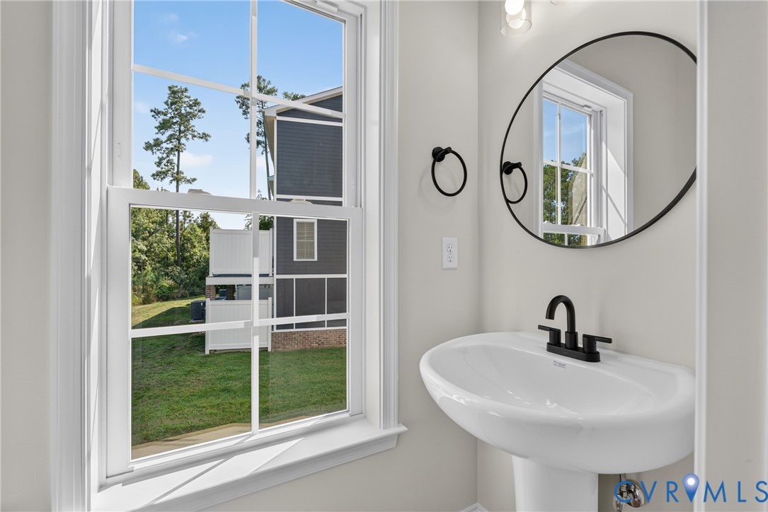 Pedestal sink with matte black faucet, framed mirror, and natural light from a double-hung window