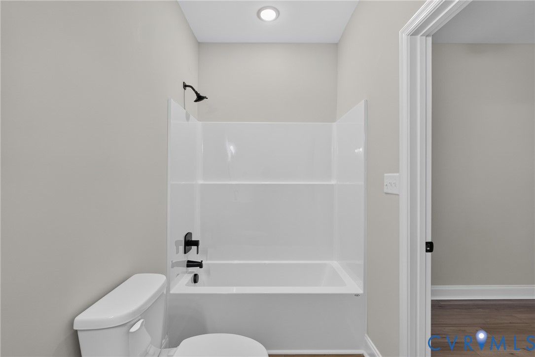 Bathtub and shower combination with matte black fixtures, white toilet, and recessed ceiling lighting