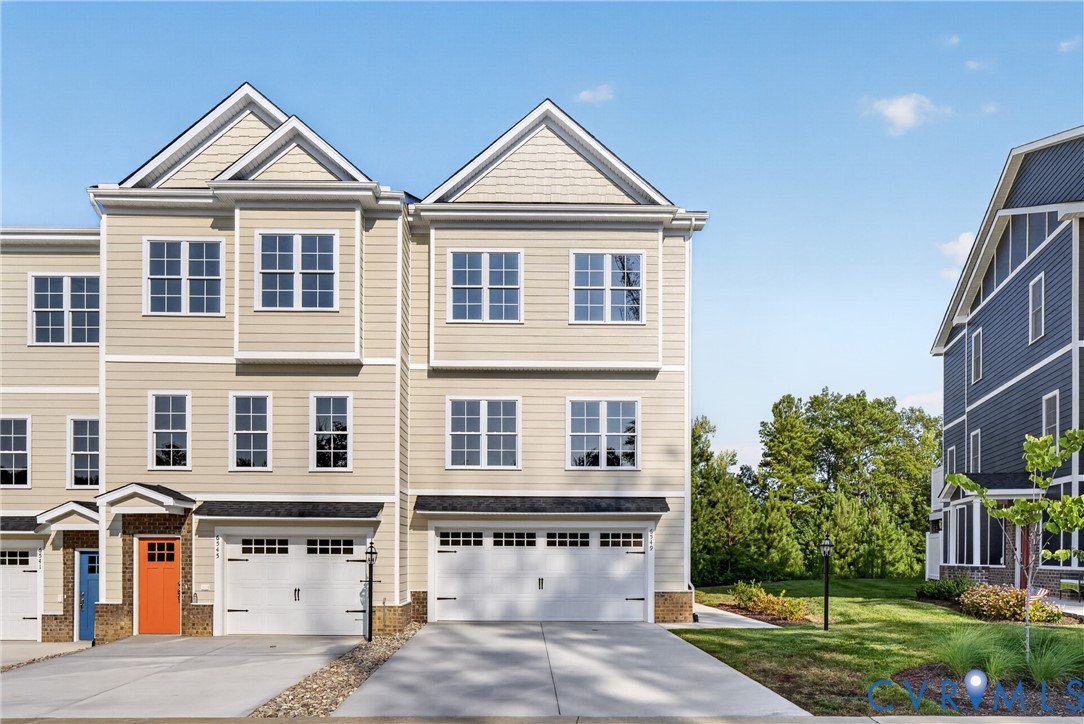 Multi-story townhome featuring light-colored siding, multiple windows, a two-car garage, and a concrete driveway Multi-story townhome featuring light-colored siding, multiple windows, a two-car garage, and a concrete driveway