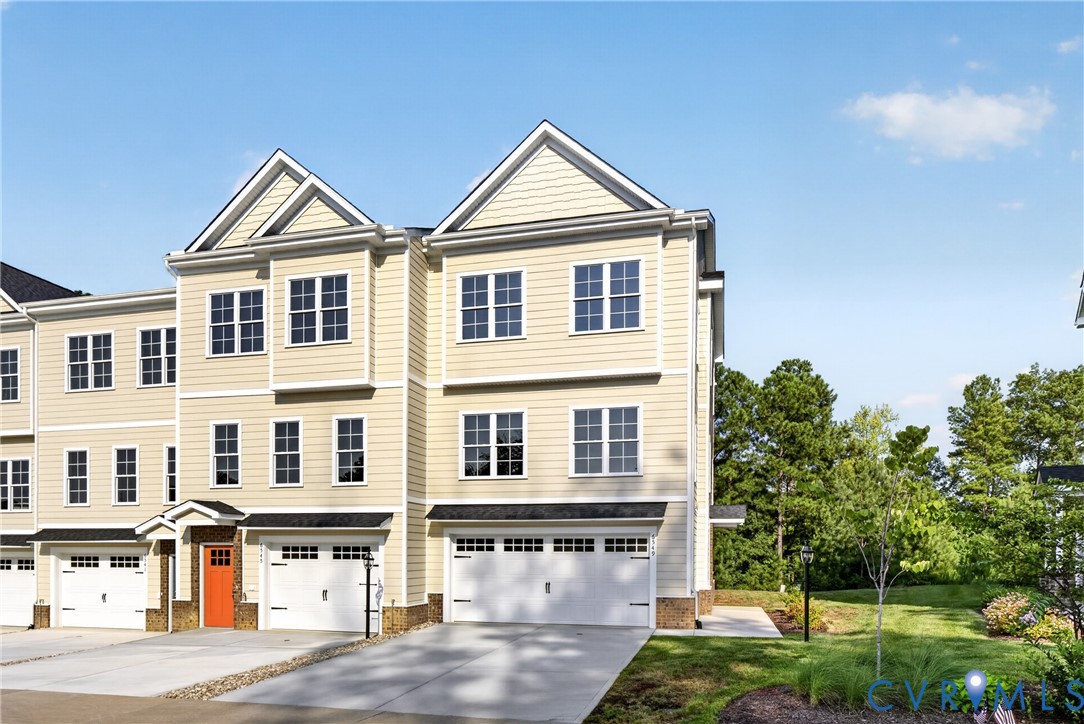 Three-story townhome with light-toned siding, attached garages, and a prominent orange entry door
